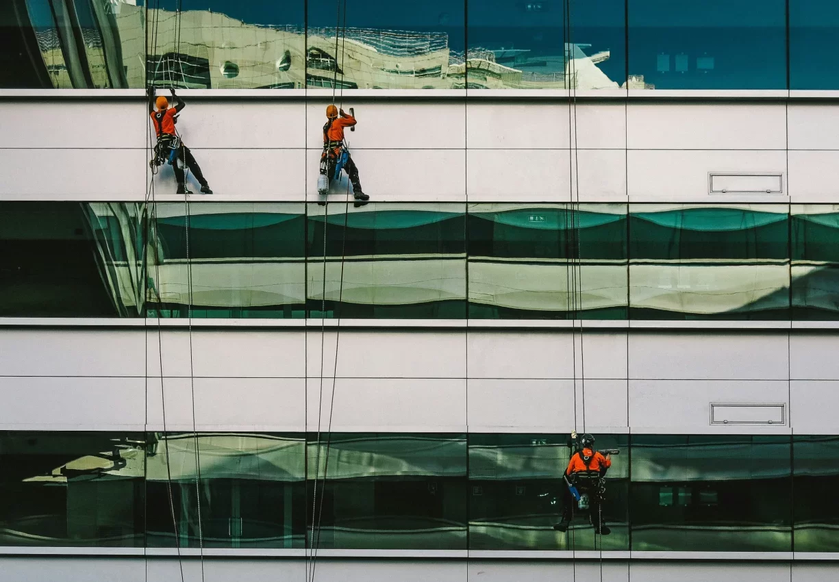 Operarios colgados de cuerdas limpiando la fachada acristalada de un edificio
