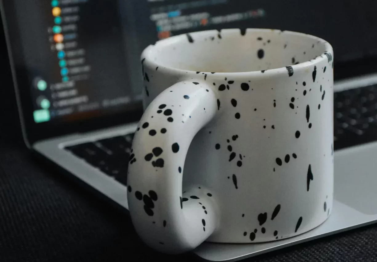 Taza de cerámica moteada delante de un portátil con código en pantalla